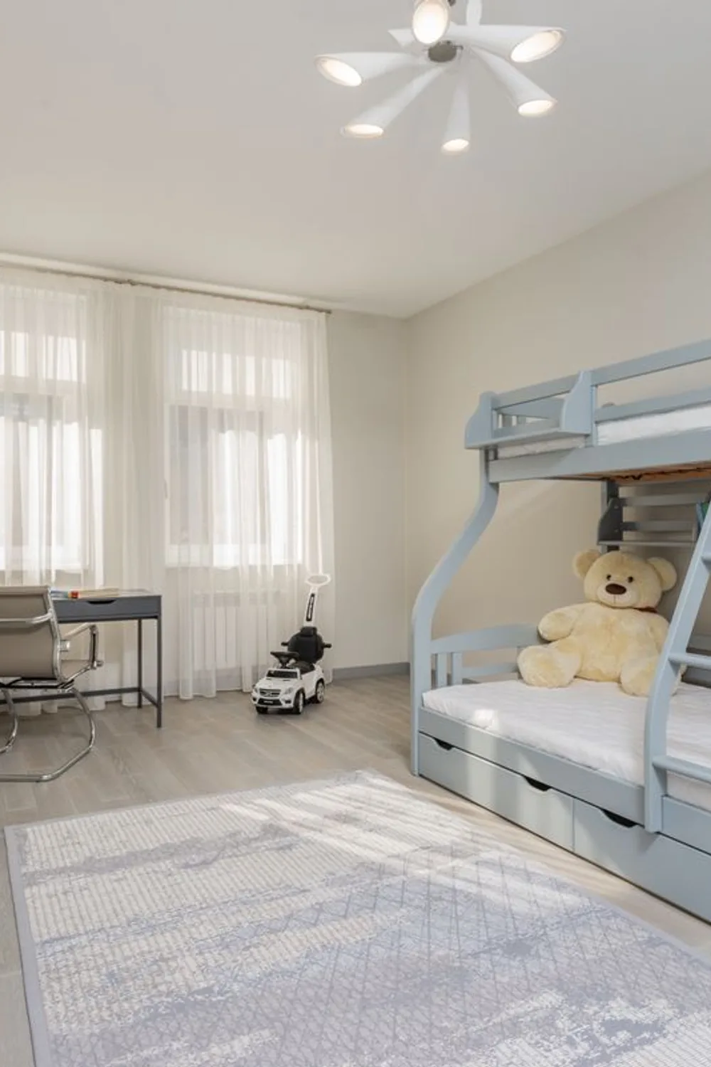 Pale blue bunk bed with under-bed drawers, open shelves, and a desk beside a bright window.